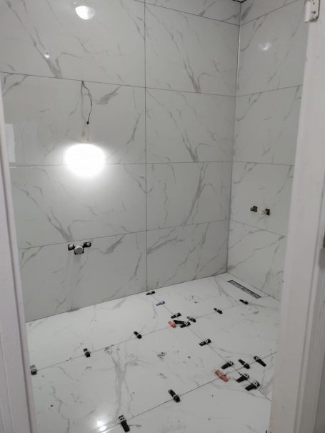 Witte marmeren badkamer met lege vloer en lichtreflecties op de muren.